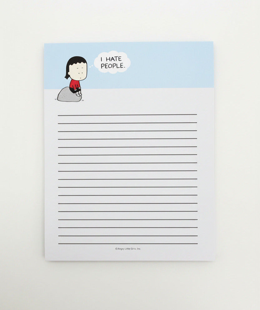 A lined notepad featuring a light blue header with a cartoon girl sitting on a rock and a speech bubble that reads 'I HATE PEOPLE.' The notepad is photographed against a plain light gray wall.
