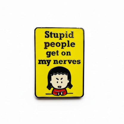 A pin with Kim, the Angry Little Asian Girl, a cartoon character and the text 'Stupid people get on my nerves' on a yellow background.